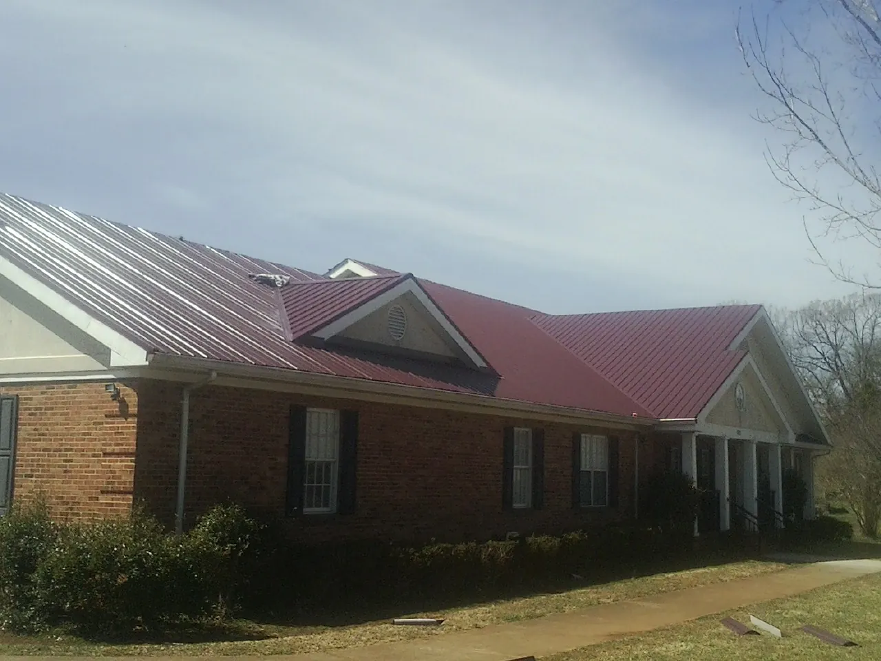 Red metal roof with gabled entries on a long brick building, from a Hail Damage Roof Repair job in Minnesota City