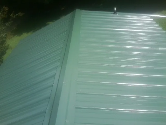 New green metal panels meeting at the ridge of a roof — Flat Roof Repair work by our crew in Minnesota City