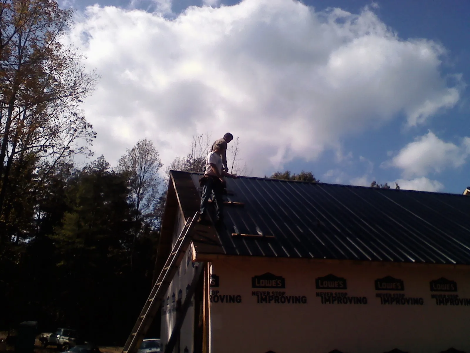 Roofer fastening dark metal panels high against a cloudy sky, from a Roof Inspection job in Minnesota City