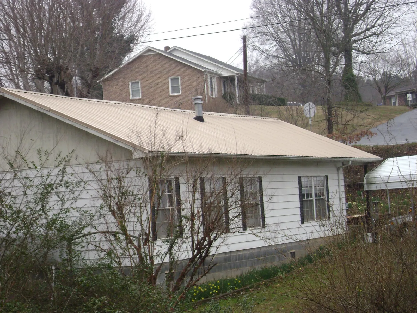 Tan metal roof on a white sided house set into a hillside — Commercial Roofing by Roofing Brothers in Minnesota City